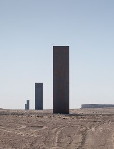 three tall metal structures in the middle of a desert