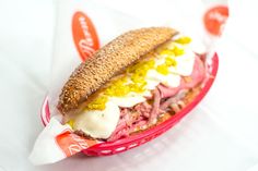 a sandwich with meat, cheese and mustard in a red basket on a white table