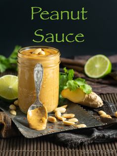 a jar filled with peanut butter next to sliced limes and peanuts on a table