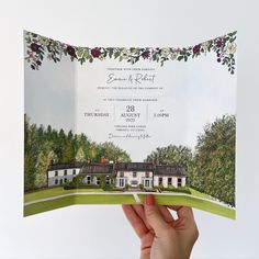 a person holding up a wedding card in front of a house with flowers on it