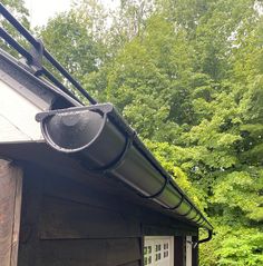 a black gutter on the side of a house with trees in the back ground