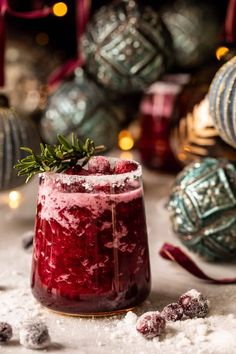 a glass filled with red liquid surrounded by christmas ornaments