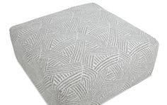 a white and grey ottoman cushion with an intricate design on the bottom, in front of a