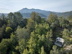 an aerial view of a cabin nestled in the woods with mountains in the back ground