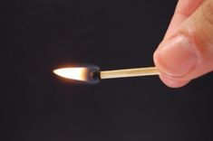 a hand holding a lit match stick in front of a black background