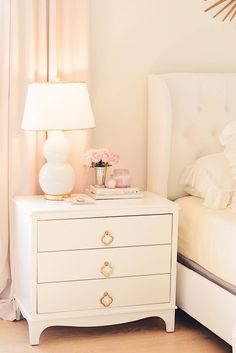 a white nightstand with flowers on it next to a bed