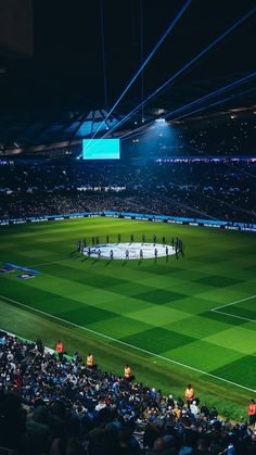 a stadium filled with lots of people standing on top of a soccer field at night