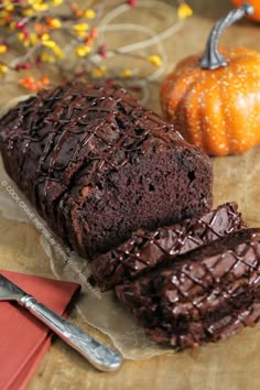 a loaf of chocolate cake sitting on top of a wooden cutting board next to two pumpkins