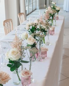 there are many vases on the table with flowers in them and wine glasses lined up next to each other