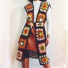 a woman is wearing a crocheted vest and boots with her hands in her pockets