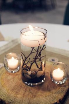 three candles are sitting on a wood slice with rocks and branches in it as centerpieces