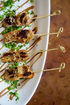 several skewered meats with sauce and garnish on a white plate