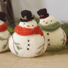 three snowmen wearing hats and scarves sitting on top of a wooden table next to pine branches