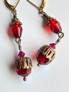 These sophisticated Victorian-inspired tiered earrings are exciting to behold, with mixed metals and ruby red colors fit for royalty! Either tier of these earrings could converted to a stand-alone shorter pair of earrings. Please message me if this possibility interests you.  Vintage 1960s red crystals with an AB finish peek out from within and below intricate textured brass bead caps, revealing surprising flashes of color when they're touched by light; semi-opaque polished red glass beads are t Nickel Free Red Crystal Earrings For Parties, Red Dangle Crystal Earrings For Anniversary, Red Garnet Dangle Earrings, Red Nickel-free Drop Crystal Earrings, Red Metal Earrings For Celebration, Red Brass Earrings With Ear Wire, Vintage Red Brass Earrings, Red Brass Drop Earrings, Festive Red Dangle Crystal Earrings