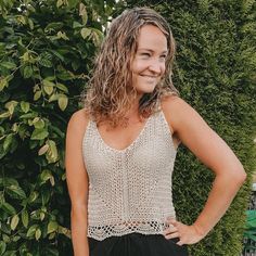 a woman standing in front of a bush with her hands on her hips and smiling