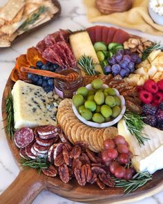 a wooden platter filled with different types of cheeses and fruit on top of a marble counter