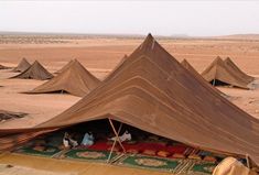 some people are sitting in the middle of a desert area with tents and rugs