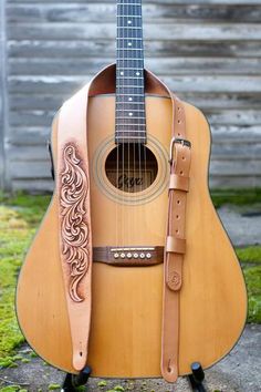 an acoustic guitar sitting on top of a wooden stand with a leather strap around it's neck