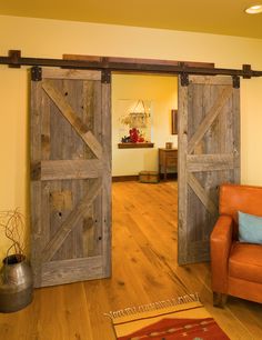 an open barn door in a living room with wooden floors and orange chair, yellow walls