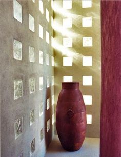 a red vase sitting on top of a wooden table next to a wall covered in squares