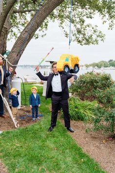 a man in a tuxedo holds up a toy truck while other people look on