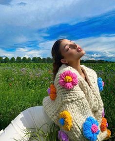 a woman laying in the grass with her eyes closed and wearing a knitted flowered sweater