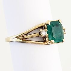 "This magnificent vintage ring boasts a lovely emerald and two diamonds set in 18K yellow gold. The emerald has a rich bluish-green color and weighs in at 1 1/4 carats. An accent diamond is set on each side of the emerald, adding elegance and sparkle. The ring has triple branched shoulders that add interest beyond the classic shank. Luxurious! Vintage: 1990s Size: 6 Materials: 18K Yellow Gold, Emerald, Diamonds Marked: 18K Emerald: 7 mm x 7mm x 4.4mm, approx. 1.25 ct. 2 Diamonds: brilliant cut, Formal Emerald Three-stone Ring, Vintage Green Emerald Ring With Brilliant Cut, Timeless Green Diamond Ring With Accents, Vintage Emerald Ring With Brilliant Cut For May Birthstone, Classic Green Emerald Ring With Diamond Accents, Vintage Emerald Cut Diamond Emerald Ring, Vintage Emerald Ring With Diamond For May Birthstone, Vintage Diamond Emerald Ring For May Birthstone, Heirloom Three-stone Emerald Ring