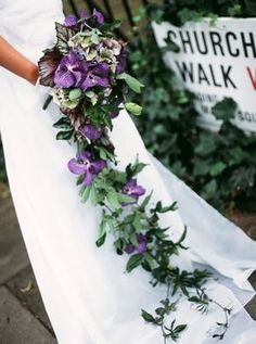 a bride holding a bouquet of flowers in her hand and wearing a white dress with purple flowers on it