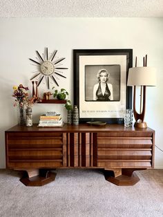 a wooden dresser sitting in front of a clock on top of a wall next to a lamp