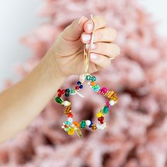 a person holding up a colorful beaded ring ornament in front of a pile of pink yarn