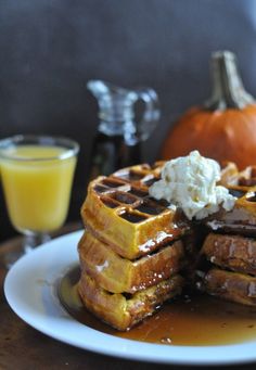 a stack of waffles sitting on top of a white plate next to a glass of orange juice