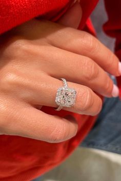 a woman's hand with a diamond ring on top of her finger and a red sweater