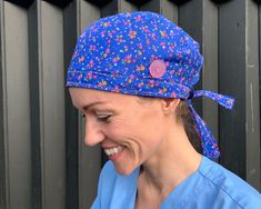 a woman in scrubs smiles while wearing a blue hat with colorful flowers on it