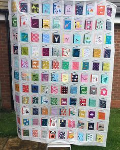 a large quilt hanging from the side of a brick building in front of a green lawn