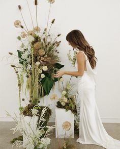 a woman in a white dress standing next to a flower display with flowers and plants