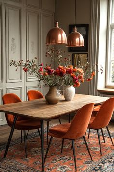 a dining room table with orange chairs and flowers in vases on top of it