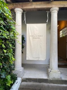 a white banner hanging from the side of a building next to some bushes and trees