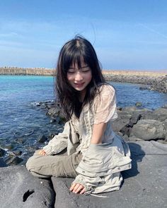 a woman sitting on top of a rock next to the ocean