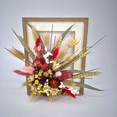 an arrangement of flowers and feathers in a wooden frame