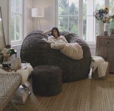 a woman laying on top of a giant bean bag chair in a living room next to a window