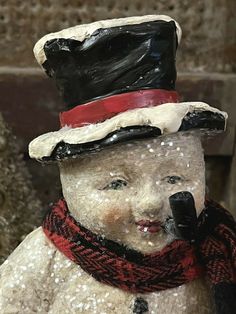 a snowman wearing a hat and scarf with a cell phone to his ear while standing in front of a stone wall