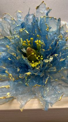 a blue and yellow flower sitting on top of a piece of wood next to a wall