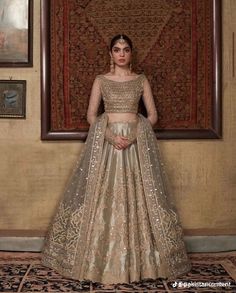 a woman standing in front of a painting wearing a gold and silver lehenga