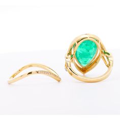 two gold rings with green stones and diamonds on the sides, one is shaped like an oval