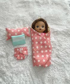 a doll in a sleeping bag on a white blanket next to a small wallet and toothbrush