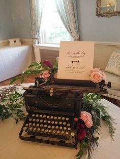 an old fashioned typewriter is set up on a table with flowers and greenery