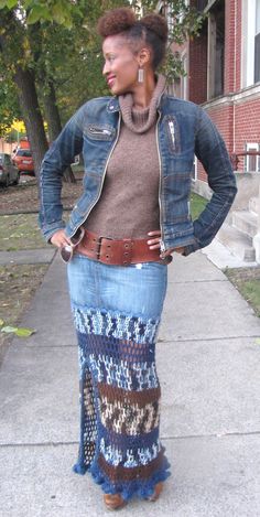 a woman standing on a sidewalk wearing a jean jacket and knitted skirt with her hands in her pockets