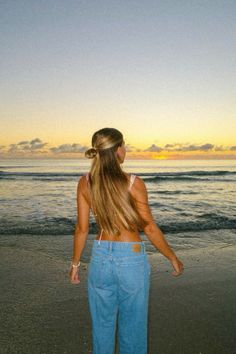 a woman standing on top of a sandy beach next to the ocean at sun set