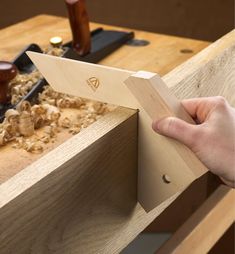 a person holding a piece of wood in front of a workbench with tools on it