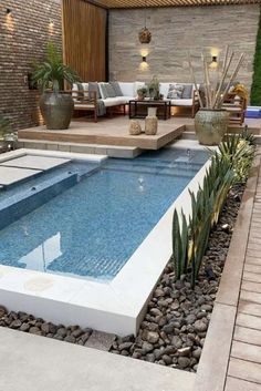 a small pool surrounded by rocks and plants in a backyard with an outdoor seating area